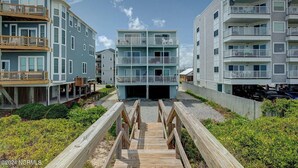 A multi-story residential building with a central entrance and a wooden deck leading to it. - Right On the Beach - Spectacular Views! (Carolina Beach)