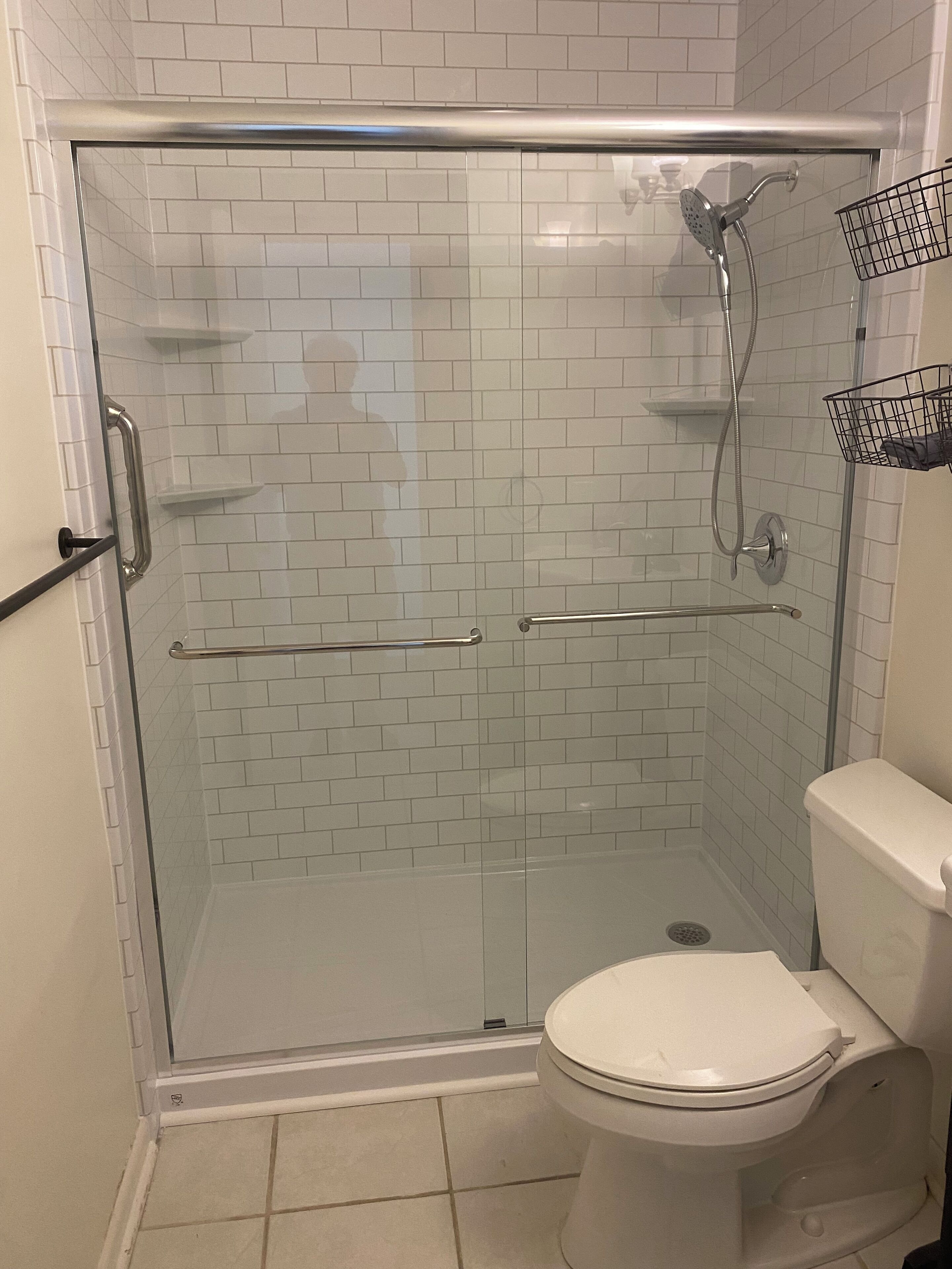 A glass-enclosed shower stall with a white toilet and a metal towel rack.
