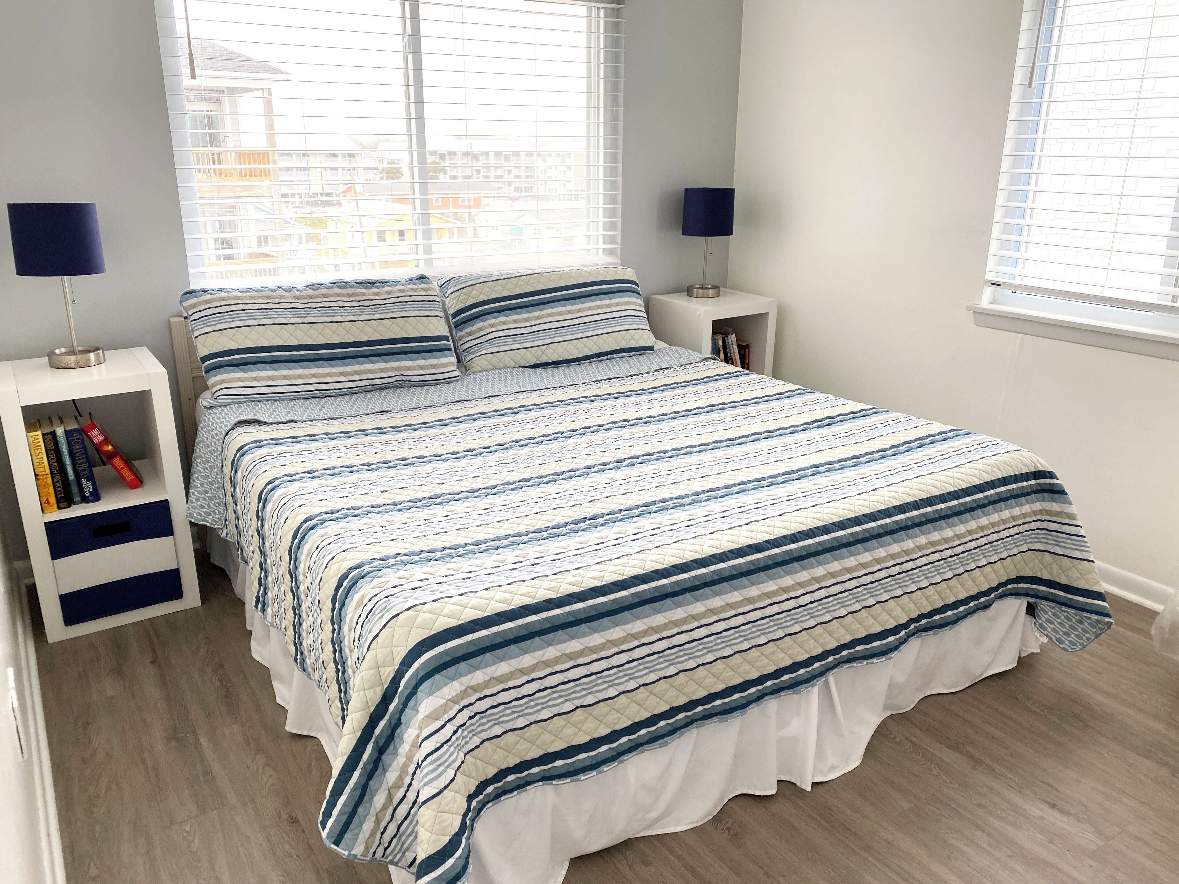 Un letto rifatto con una coperta a righe, due comodini con lampade e una libreria piena di libri.