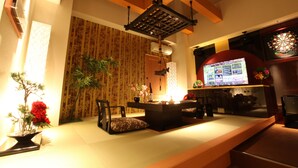 A traditional Japanese-style living room with tatami flooring, a low wooden table, a sofa, a decorative plant, and a television. - LUSSO CROCE ASIAN RESORT - Adult Only (Yokohama)