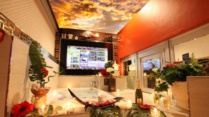 A luxurious bathroom with a large bathtub, a television screen, and various amenities like flowers and candles. - LUSSO CROCE ASIAN RESORT - Adult Only (Yokohama)