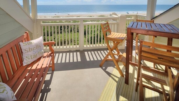 A wooden deck with a bench and a table, overlooking a beach. - OIBV 716 - Island Dream: Oceanfront condo in Oak Island, perfect for family getaways! (Oak Island)