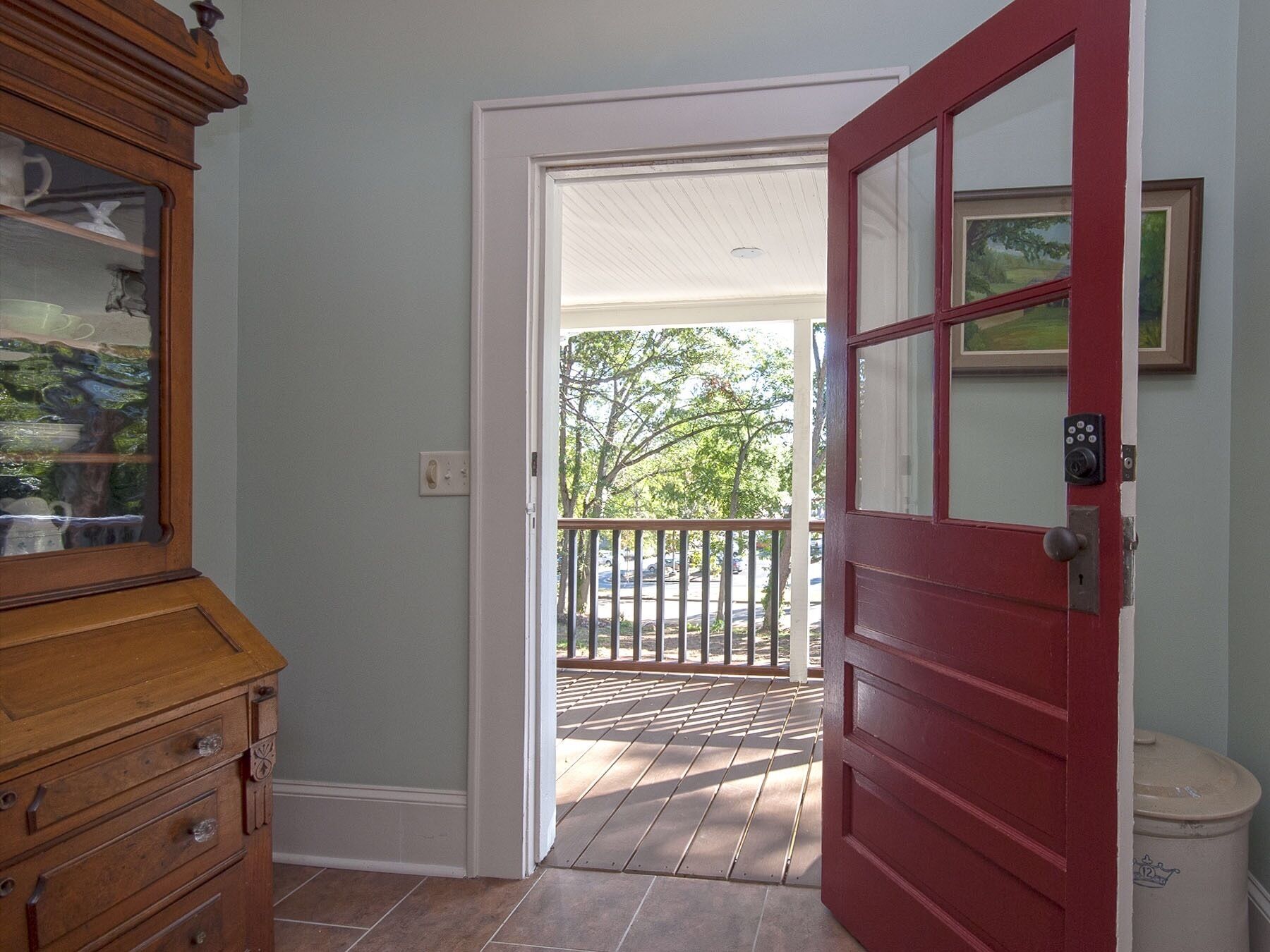 A wooden dresser with drawers, a red door, and a view of a balcony with a railing.