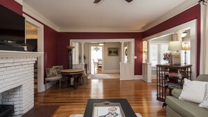 A spacious living room with a fireplace, a ceiling fan, and a dining area with a table and chairs.
