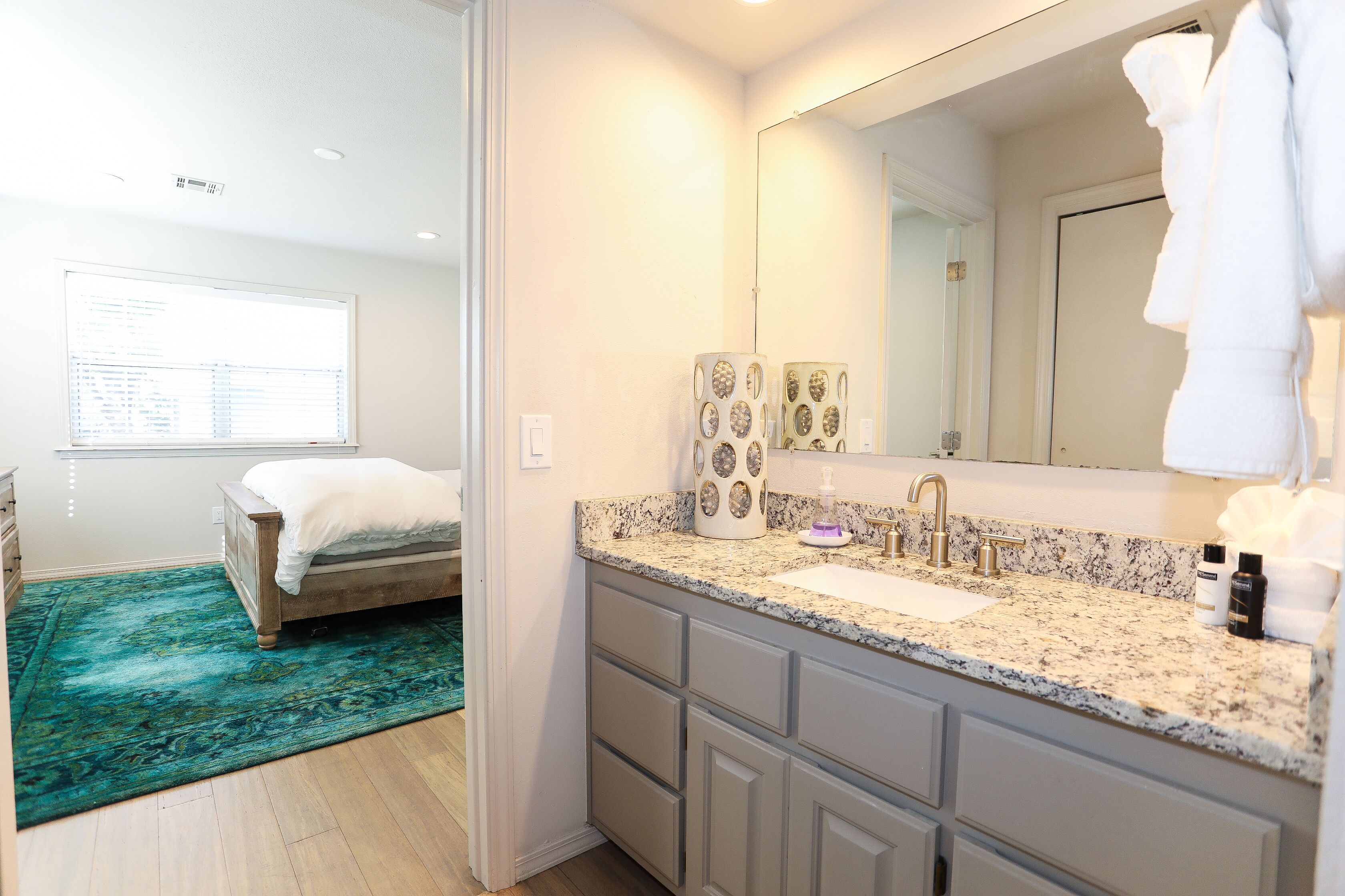 Une salle de bain avec un comptoir en granit, un grand miroir, un lavabo et un porte-serviettes.