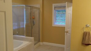 A bathroom with a glass shower enclosure, a bathtub, and a window with a view of greenery. - Beautiful Mountain views with private balcony close to Asheville, NC (Barnardsville)
