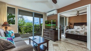 A spacious bedroom with a large bed, a TV, and a balcony with a view of greenery.