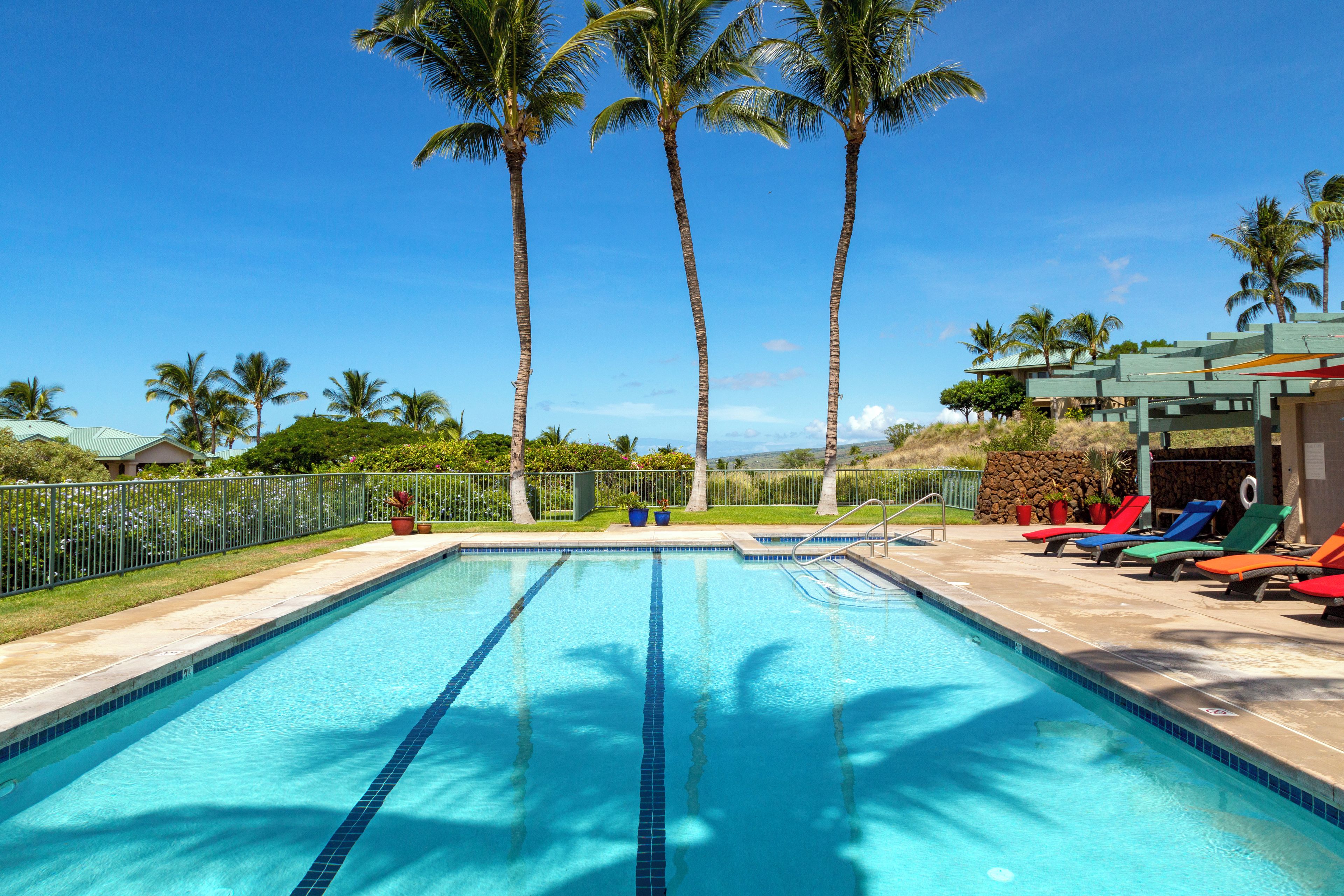 A swimming pool with clear blue water, surrounded by palm trees and a lounge area with colorful sun loungers.