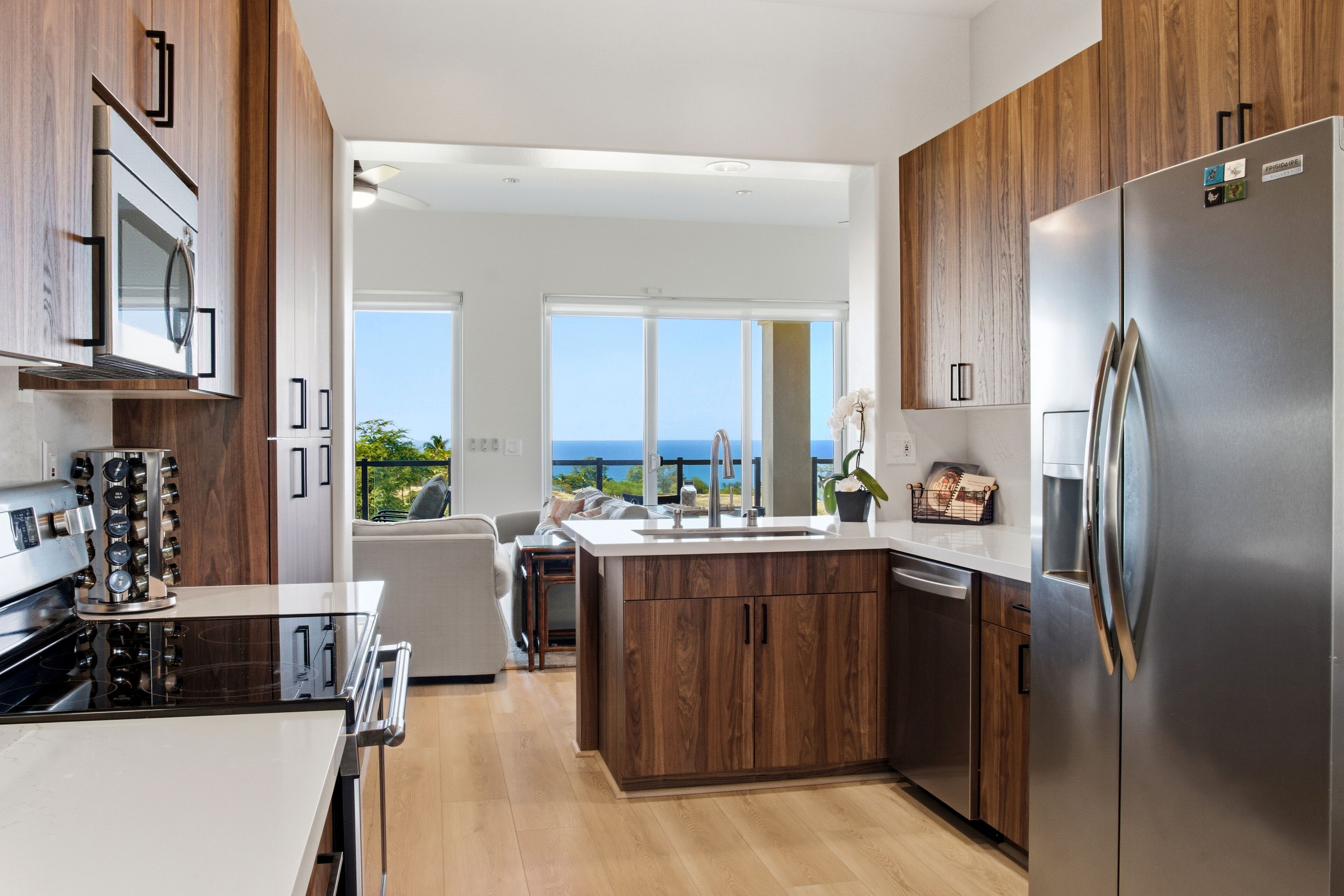 A modern kitchen with a large island, stainless steel appliances, and a view of the ocean.