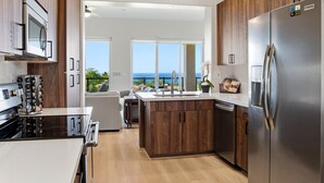 A modern kitchen with a large island, stainless steel appliances, and a view of the ocean. - NEWLY RENOVATED Popular Mauna Kea Condo - Spectacular Panoramic Ocean Views (Waimea)