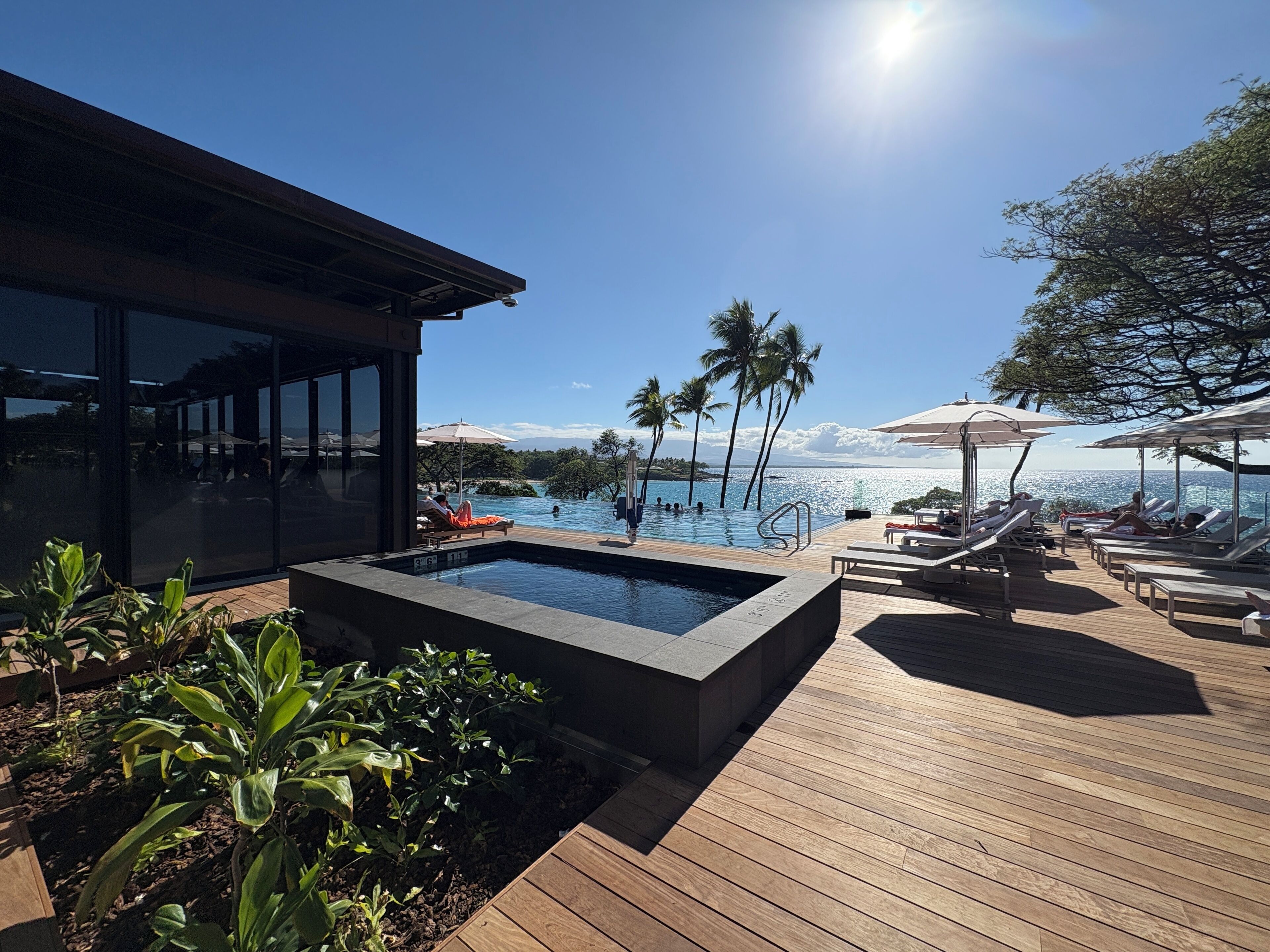 A pool area with lounge chairs and a view of the ocean.