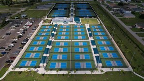 Ilmakuva urheilukeskuksesta, jossa on useita tenniskenttää, parkkipaikka ja sitä ympäröivä asuinalue.
