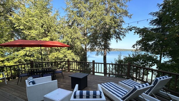 Una terraza con mobiliario de mimbre, un paraguas rojo y vistas al lago.