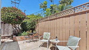 Eine Terrasse im Freien mit zwei weißen Metallstühlen und einem kleinen runden Tisch, einem Holzzaun sowie einem Holzboden mit einem Ziegelpflanztopf.