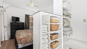 Ein Schlafzimmer mit Bett, Fernseher, Kleiderschrank und einer Regalwand mit Handtüchern und Körben.