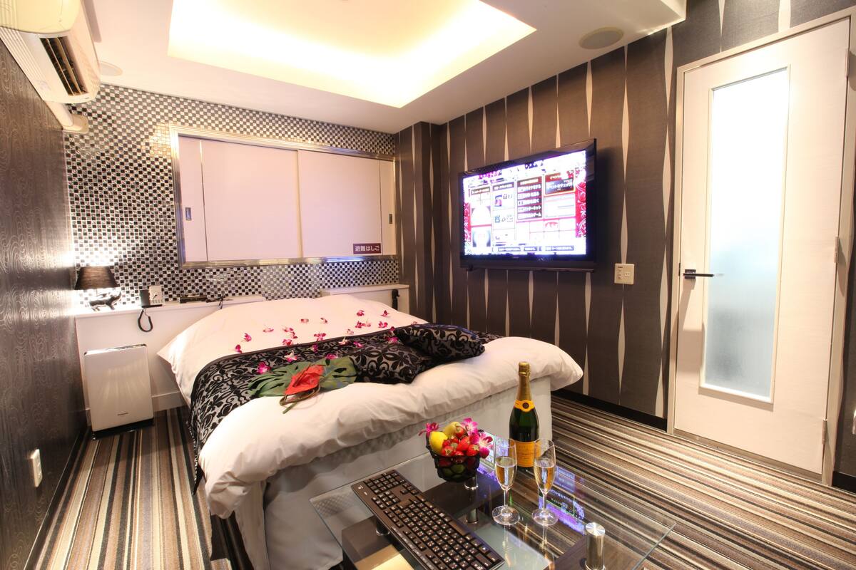 Une chambre d’hôtel équipée d’un lit, d’une télévision, d’un minibar et d’un bureau avec un clavier et une bouteille de champagne.