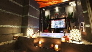A modern bar area with a large screen displaying content, a bar counter with candles, and a decorative plant.