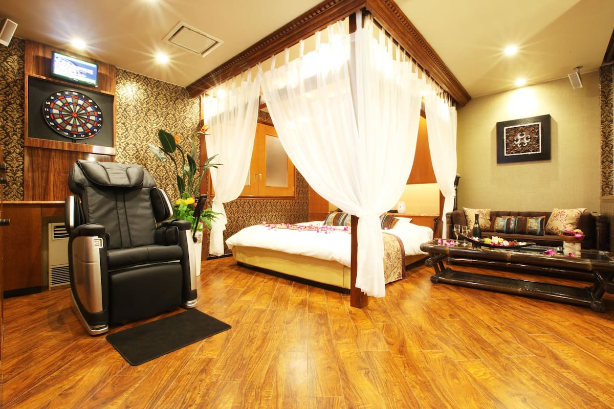 A room with a four-poster bed, a massage chair, a television, and a dartboard.