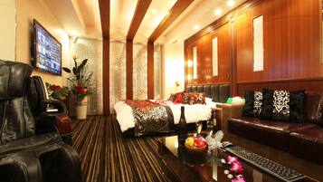 A hotel room with a bed, a sofa, a massage chair, a desk with a keyboard, and a TV on the wall.