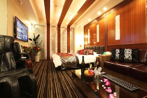 A hotel room with a bed, a sofa, a massage chair, a desk with a keyboard, and a TV on the wall.