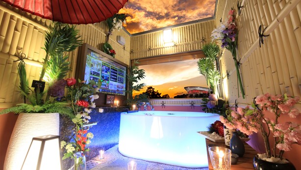 A spa area with a hot tub, surrounded by plants and flowers, and a sunset view through a window. - HOTEL GRASSINO URBAN RESORT URAWA - Adult Only (Saitama)