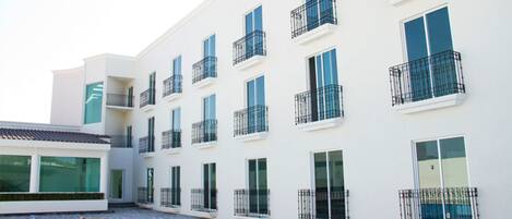 A modern building with multiple balconies and large windows, a swimming pool, and a flat roof.