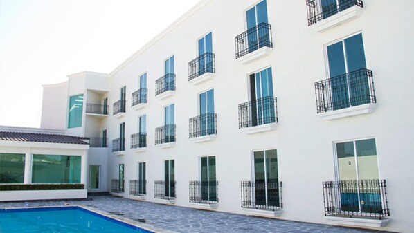 Um edifício moderno com várias varandas e grandes janelas, piscina e telhado plano.