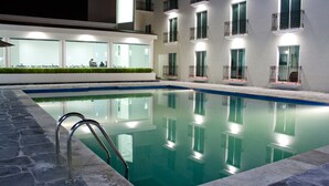 A swimming pool with a metal ladder, surrounded by a building with multiple balconies and windows. - Hotel Osalle Inn (Chignahuapan)