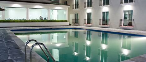 A swimming pool with a metal ladder, surrounded by a building with multiple balconies and windows.