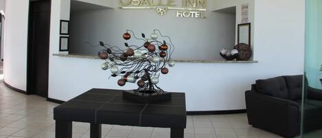 Zona de recepción con diseño moderno, que incluye un mostrador de recepción, una escultura metálica decorativa y un cartel del Hotel Osalle Inn.