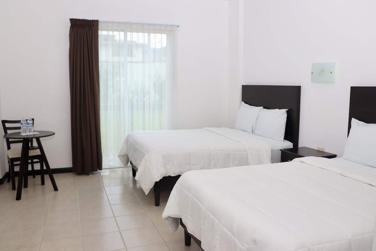 Una habitación de hotel con dos camas individuales, una mesita con una silla y una ventana con cortinas.
