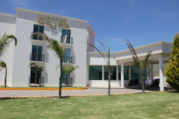 A modern hotel with a prominent "HOTEL" sign, multiple balconies, and a well-maintained lawn with palm trees.