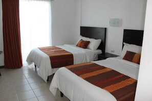 A hotel room with two beds, each with a striped bedspread and matching pillows. There is a nightstand between the beds, and a window with curtains on the left side. - Hotel Osalle Inn (Chignahuapan)