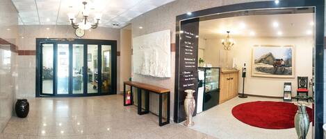 A hotel lobby with a reception desk, a red carpet, and a large abstract painting on the wall.