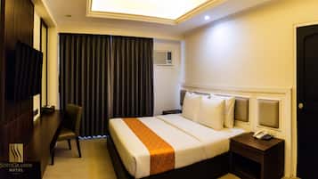 A hotel room with a bed, bedside table, chair, and a desk with a telephone.
