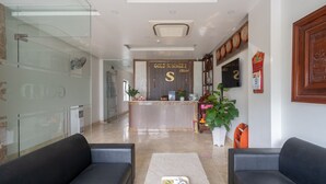 Un espace d’accueil d’hôtel comprenant un comptoir de réception, un coin salon et un mur en verre.