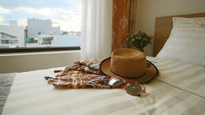 Un lit avec une couvre-lit à rayures, un chapeau de paille, une paire de lunettes de soleil et une écharpe à motifs.