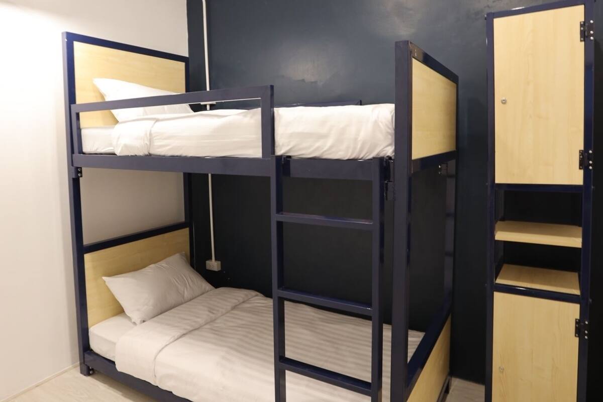 A bunk bed with a wooden ladder, a small wooden cabinet, and a white lamp.