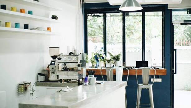 A modern kitchen with a coffee machine, shelves with colorful mugs, and a view through a large window. - Local Time Bangkok - Hostel (Bangkok)