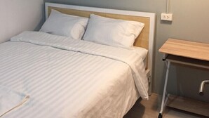 A neatly made bed with white linens, a wooden headboard, and a bedside table with a lamp. - Local Time Bangkok - Hostel (Bangkok)