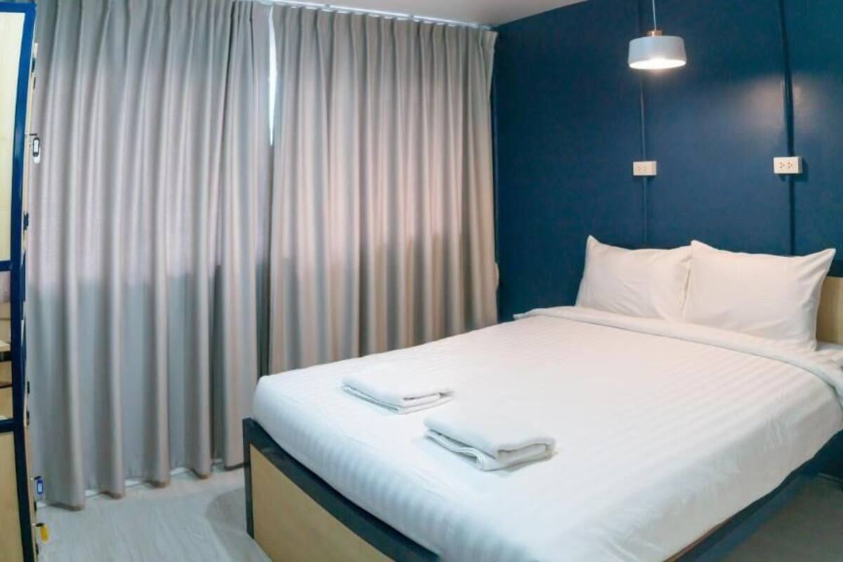 A hotel room with a bed, curtains, a desk, and a wall-mounted light fixture.