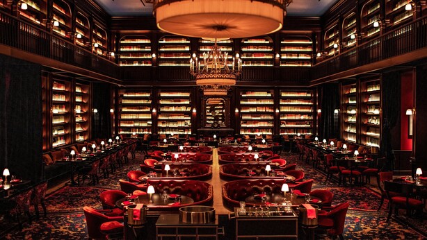 A grand library with rows of bookshelves, a central chandelier, and red upholstered seating areas. - The Reserve at Park MGM (Las Vegas)