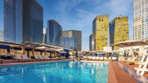 A pool area with lounge chairs and umbrellas, surrounded by modern high-rise buildings. - The Reserve at Park MGM (Las Vegas)