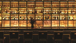 A bar with multiple shelves of liquor bottles, a central plant, and several bar stools. - The Reserve at Park MGM (Las Vegas)