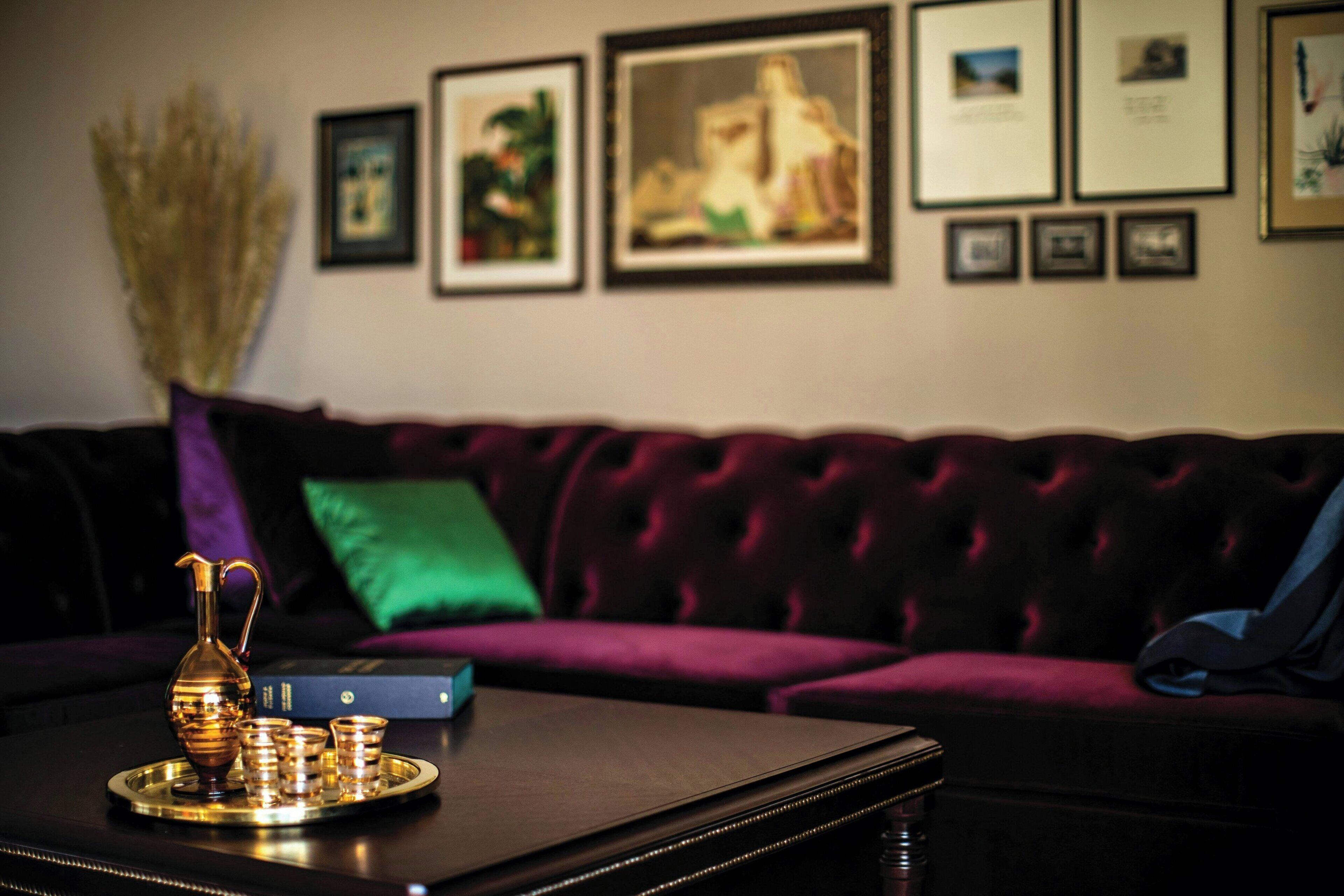 A room with a dark wooden coffee table, a purple sofa, and framed pictures on the wall.
