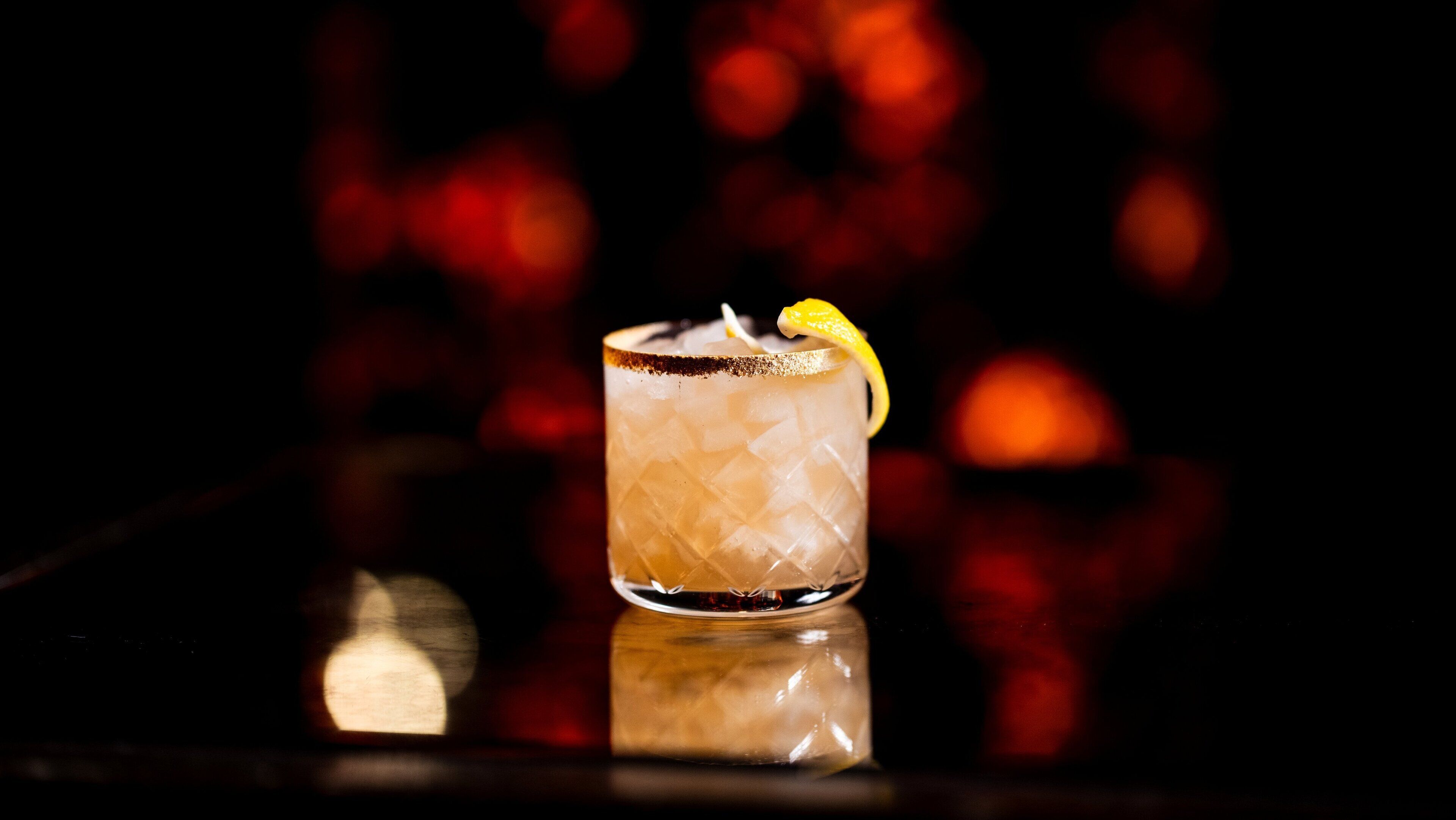 A glass of iced drink with a lemon garnish on a reflective surface.