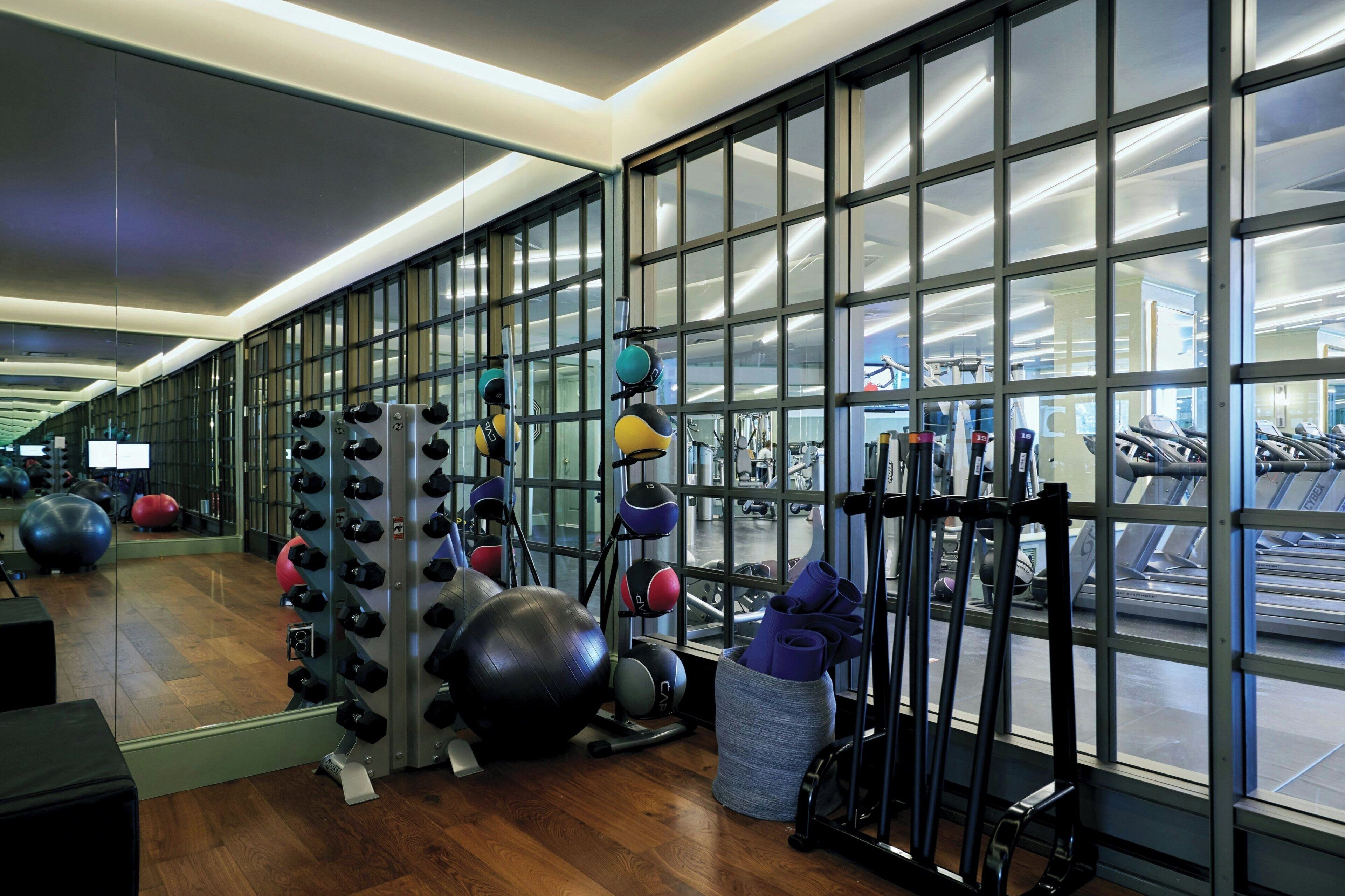 Un gimnasio con equipo de ejercicio, ventanas amplias y suelo de madera.