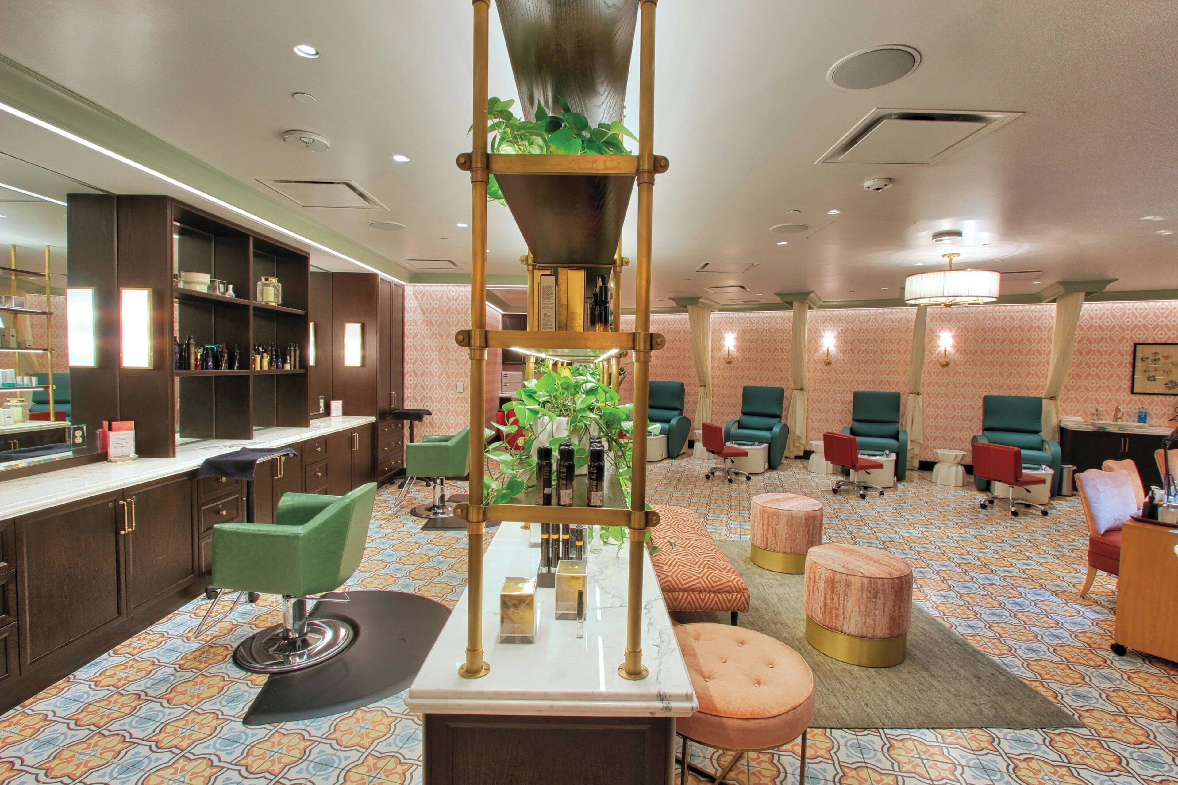 Un hall d’hôtel moderne, agrémenté d’une grande installation végétale au centre, de plusieurs espaces de détente et d’un bar dont les étagères sont remplies de produits de toilette.