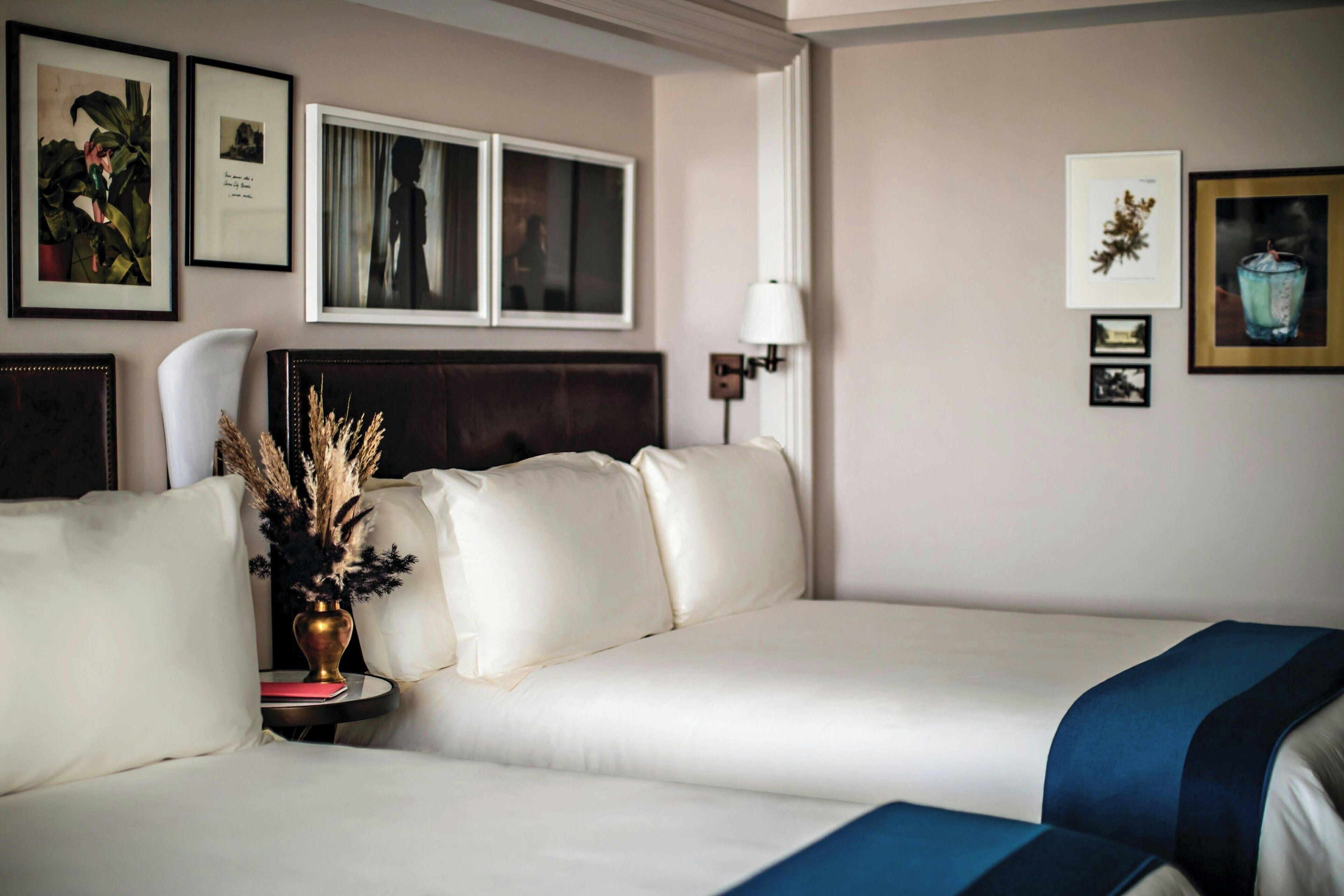 A hotel room with a white sofa, a small side table with a vase, and a lamp. There are framed pictures on the wall.