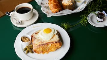 A breakfast setting with a croissant, a cup of coffee, and a plate with a fried egg and pickles.